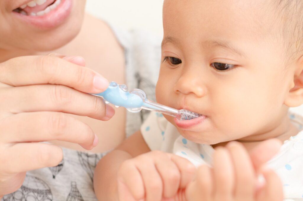 Mom helping toddler brush teeth with white spots