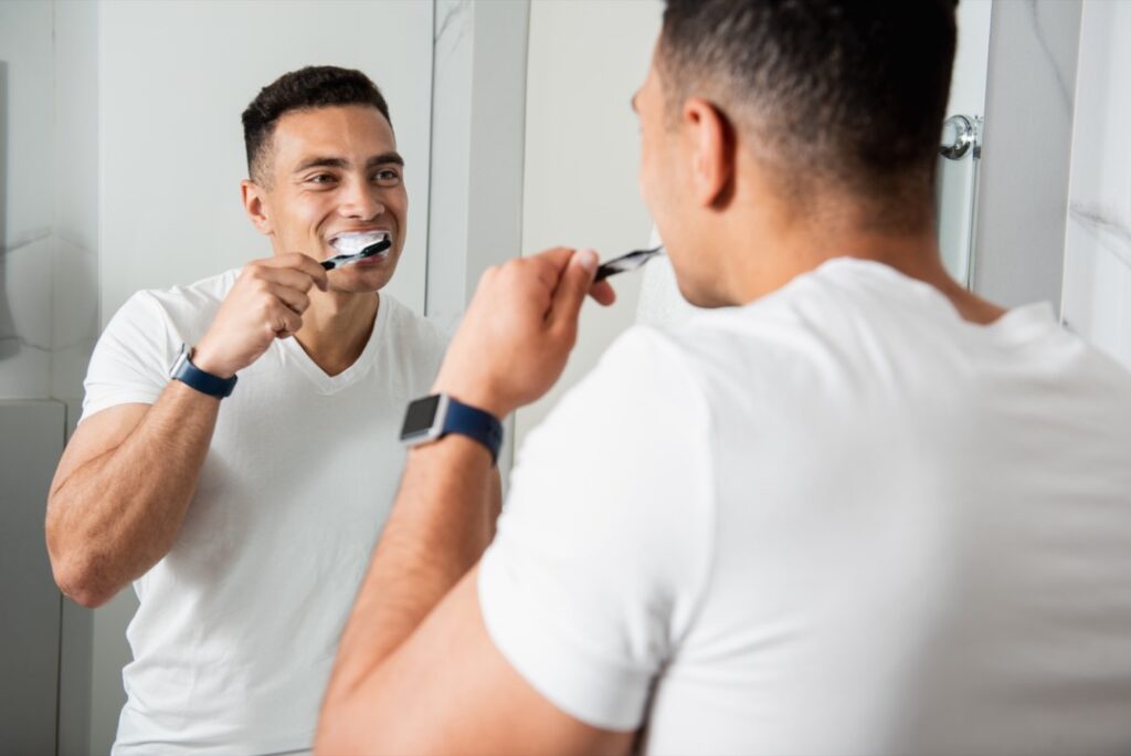 Young man looking in the mirror while brushing his teeth
