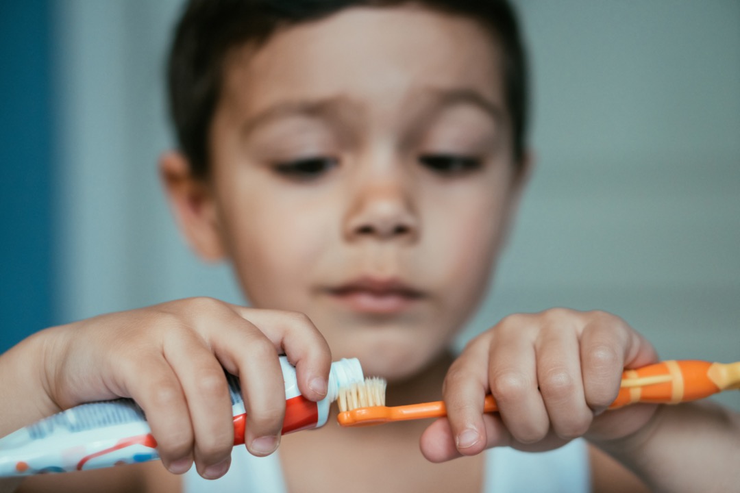 Young boy putting toothpaste on toothbrush